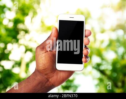 Hand shows mobile smart phone, nature blurred background Stock Photo