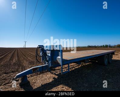 Agricultural trailer in ploughed field and electricity cable poles leading into the distance, East Lothian, Scotland, UK Stock Photo