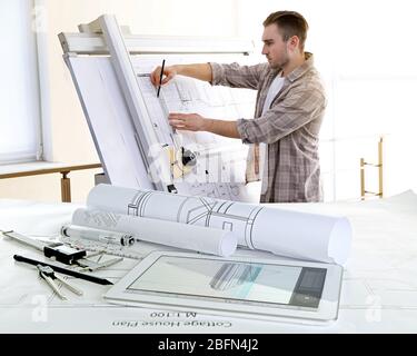 Table with construction drawings and male architect working on blueprints Stock Photo