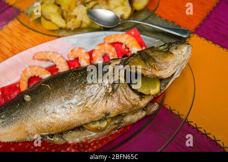 cooked sea bass on a glass dish and a plate with baked potato garnish Stock Photo