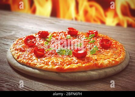Tasty pizza with cherry tomatoes on wooden table against fire flame background Stock Photo