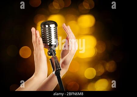 Retro microphone in female hands on abstract blurred background Stock Photo