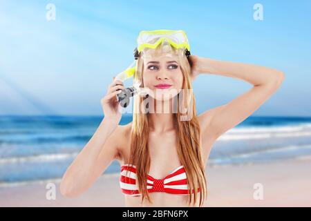 Young beautiful woman in red striped swimsuit and diving mask on blurred sea background Stock Photo