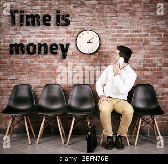 Young businessman sitting on a chair and talking on smart phone in brick wall hall Stock Photo