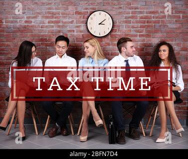 Text Tax Time and young people sitting on a chairs in brick wall hall Stock Photo