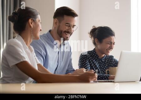 Diverse colleagues feels overjoyed laughing sit at workplace Stock Photo