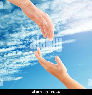 Female and male hands reaching to each other on sky background. Help and care concept. Stock Photo