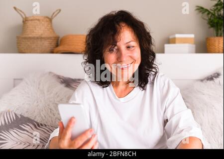 Charming, pretty, stylish, modern grandmother sitting on sofa in living room at home, doing online shopping through 3G internet, having smart phone in hands. Copy space. Soft focus  Stock Photo