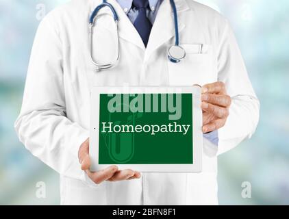 Doctor hands holding tablet with word HOMEOPATHY on screen. Alternative medicine concept. Stock Photo