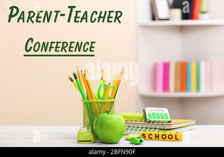 Apple with stationery on white wooden table. Text PARENT-TEACHER CONFERENCE on blurred background. School concept. Stock Photo