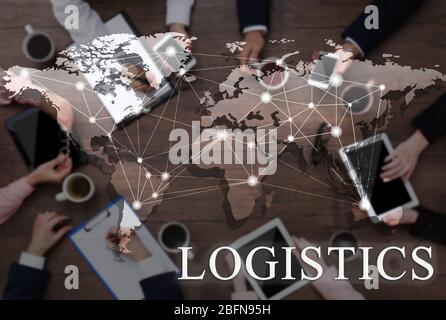 Word LOGISTICS and world map on background. People working at table, closeup. Business concept. Stock Photo