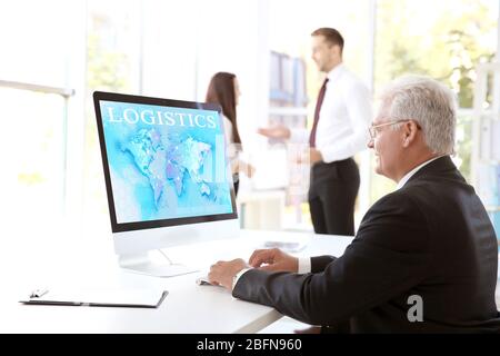 Man working with computer at office. Word LOGISTICS and world map on monitor. Business concept. Stock Photo