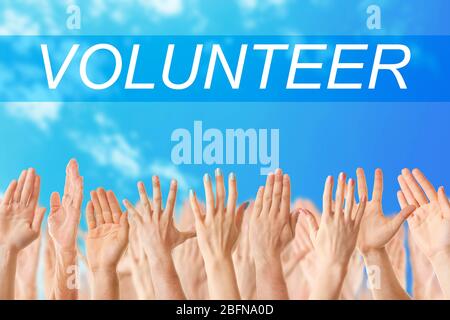 Hands and word VOLUNTEER on blue sky background. Help and support concept. Stock Photo