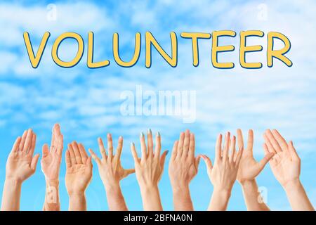 Hands and word VOLUNTEER on blue sky background. Help and support concept. Stock Photo