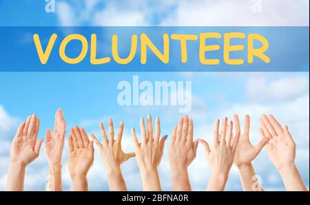 Hands and word VOLUNTEER on blue sky background. Help and support concept. Stock Photo