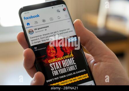 A man's hand holding a smartphone showing a British HM Government advert on Facebook warning the public to stay at home because of Covid 19, UK Stock Photo