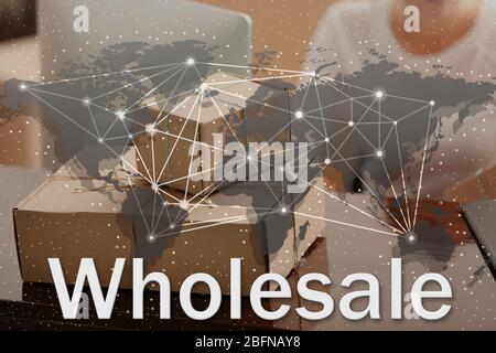 World map and word WHOLESALE on background. Cardboard boxes at storehouse. Wholesale and logistics concept. Stock Photo