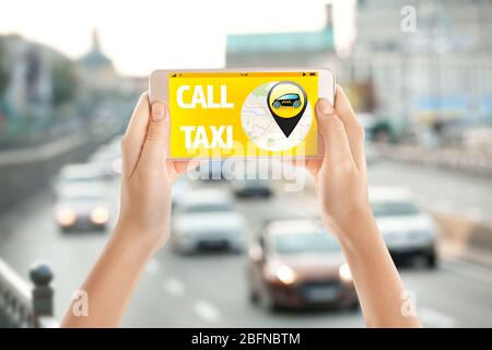 Female hands with smartphone on cityscape background. Taxi service application on screen. Stock Photo