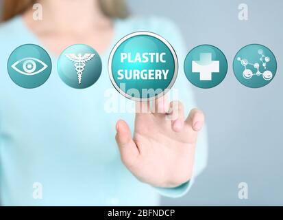 Woman pushing PLASTIC SURGERY button on virtual screen Stock Photo