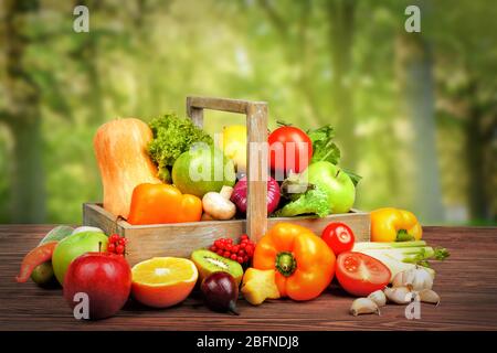 Fresh vegetables and fruits on wooden table against nature background Stock Photo