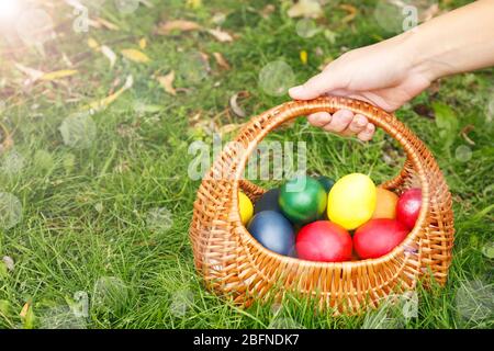 Female hand holding basket with Easter eggs on green grass Stock Photo