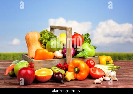 Fresh vegetables and fruits on wooden table against nature background Stock Photo