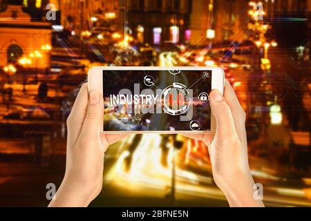 Female hands with smartphone on cityscape background. Text INDUSTRY 4.0 on screen Stock Photo