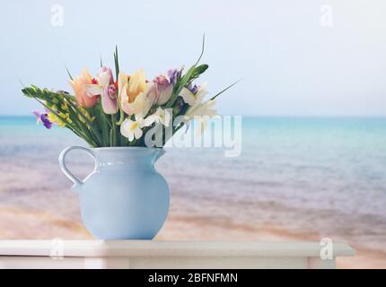 Beautiful bouquet in jug on table against seascape background Stock Photo