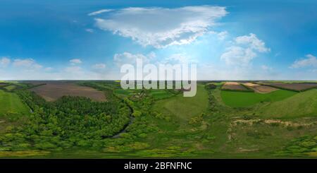 360 degree panoramic view of Panorama aerial view of green meadow and field, white clouds with a blue sky with a country road leading to the forest and lake.