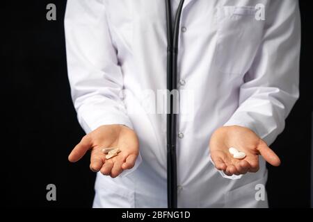 Cropped view of female Doctor holding in hands Pills to choose. Difficult Choice between drugs. Placebo drugs concept. Healthcare concept. Stock Photo