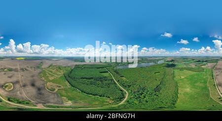 360 degree panoramic view of Panorama aerial view of green meadow and field near the path. gray and white clouds with a blue sky with a country road leading to the forest