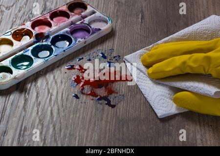 A hand in a yellow protective glove wipes the stain from the paints with a paper towel, a napkin.The woman does the cleaning. Clean, house, housekeepe Stock Photo