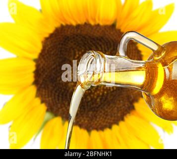 Pouring cooking oil from glass jug and sunflower on background Stock Photo