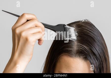 Closeup woman hands dyeing hair using a black brush. Colouring of white hair at home. Stock Photo