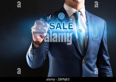 Man writing word SALE on virtual screen against dark background Stock Photo