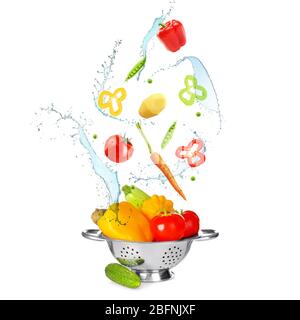 Different vegetables, water splashes and colander on white background Stock Photo