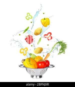 Different vegetables, water splashes and colander on white background Stock Photo