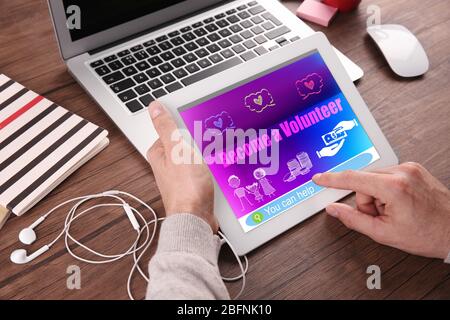 Woman using tablet with text BECOME A VOLUNTEER on screen at table Stock Photo