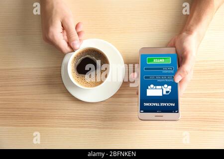Woman tracking parcel with help of smartphone app at table Stock Photo