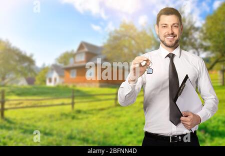 Real estate agent holding key in front of country house outdoors Stock Photo