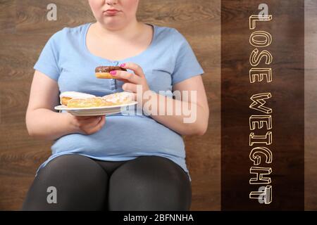Motivation quote LOSE WEIGHT and overweight woman eating sweets on wooden background Stock Photo