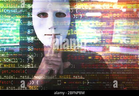 Hacker in mask showing silence gesture and code on blurred background. Concept of cyber attack and security Stock Photo
