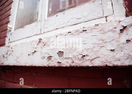 View of an old red and white building window with flaky chipped paint on the wood and bricks. Vintage window with flaky paint coming off. Stock Photo
