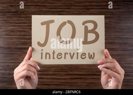 Labor market concept. Female hands holding paper with text JOB INTERVIEW on wooden background Stock Photo