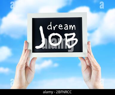 Labor market concept. Female hands holding chalkboard with text DREAM JOB on sky background Stock Photo