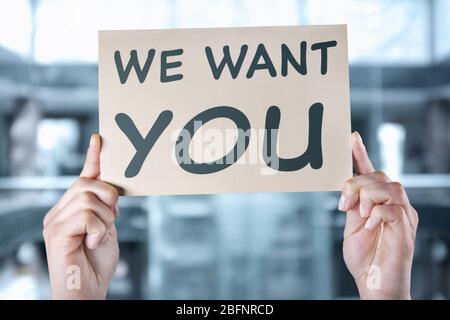 Labor market concept. Female hands holding paper with text WE WANT YOU on blurred office background Stock Photo