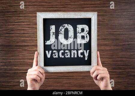 Labor market concept. Female hands holding chalkboard with text JOB VACANCY on wooden background Stock Photo