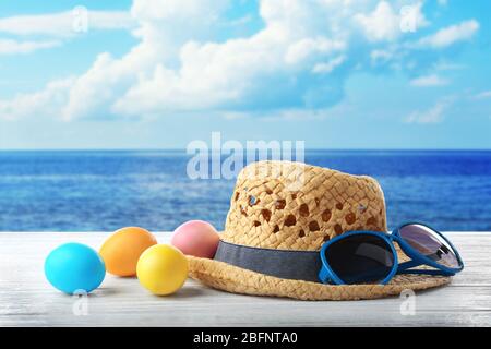 Easter eggs with hat and sunglasses on wooden table at shore Stock Photo