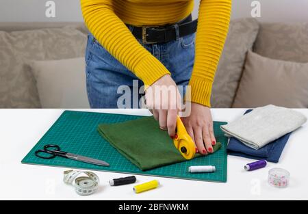 woman in a yellow cuts the fabric. there are quilting tools on the table. patchwork knife, scissors, lined cutting mat, self-locking, thread, centimet Stock Photo