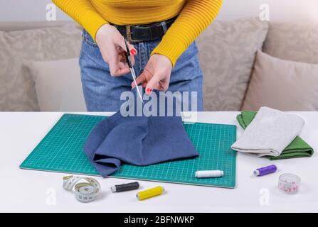 woman in a yellow cuts the fabric. there are quilting tools on the table. patchwork knife, scissors, lined cutting mat, self-locking, thread, centimet Stock Photo